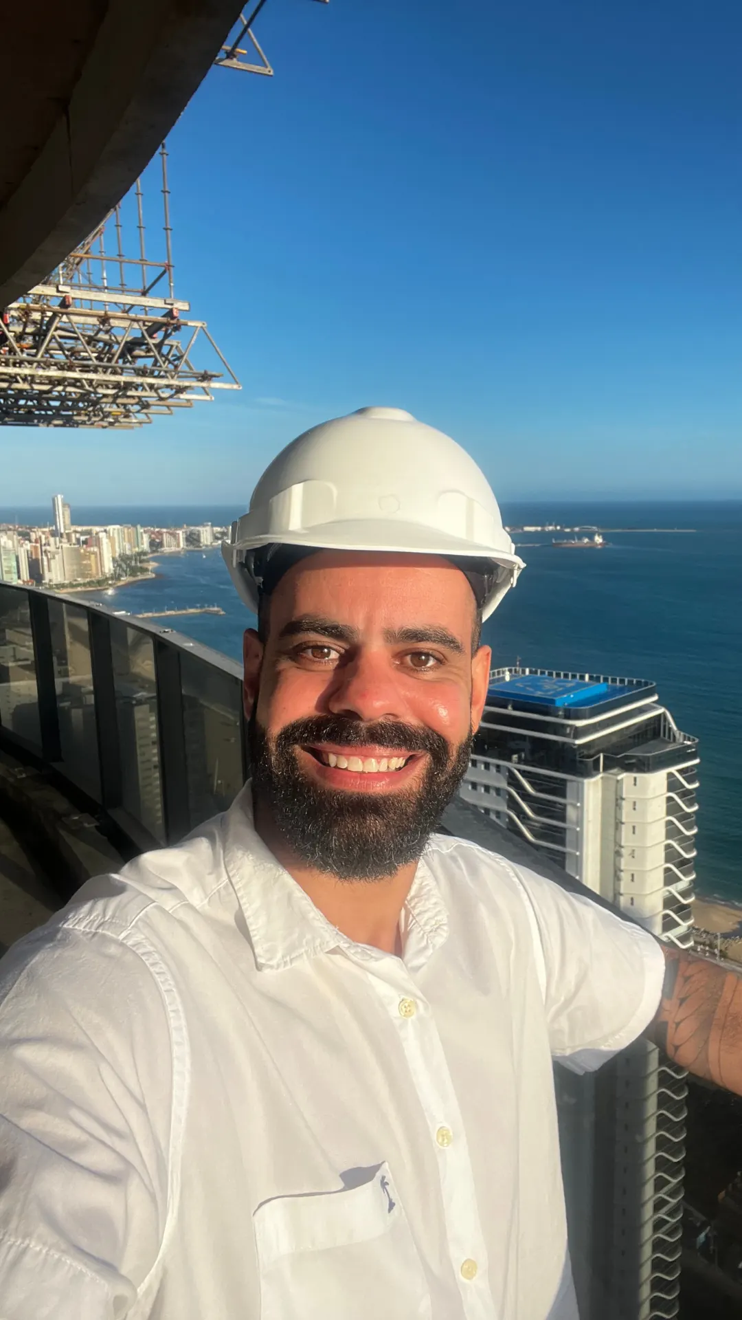 Selfie do fundador da ROTNA de capacete em uma obra, com a cidade e o mar ao fundo.